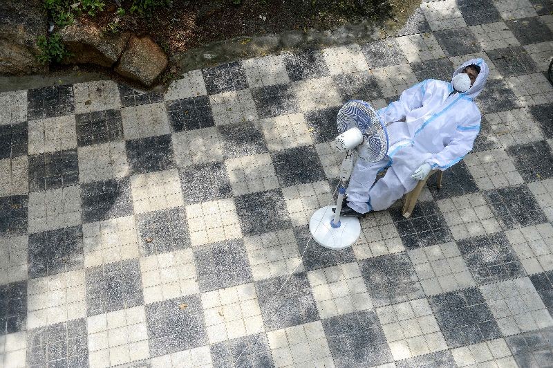 A health worker wearing a Personal Protective Equipment (PPE) suit takes a break sitting in front of a fan while waiting for to collect swab samples from residents for Covid-19 coronavirus tests at a public health centre in Hyderabad on September 17, 2020. (Photo by Noah Seelam/AFP Photo)